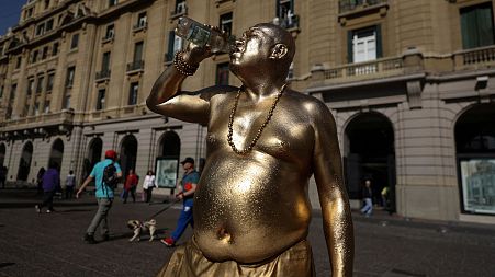 A human living statue drinks from a bottle as he takes a break during an unusual winter period heatwave in Santiago, Chile, 4 August 2023.