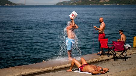 People cool off at the Bosphorus as forest fire smoke rises, background, during a hot summer day in Istanbul, Turkey, July 2023. 